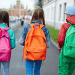32134289 – backs of schoolkids with colorful rucksacks moving in the street